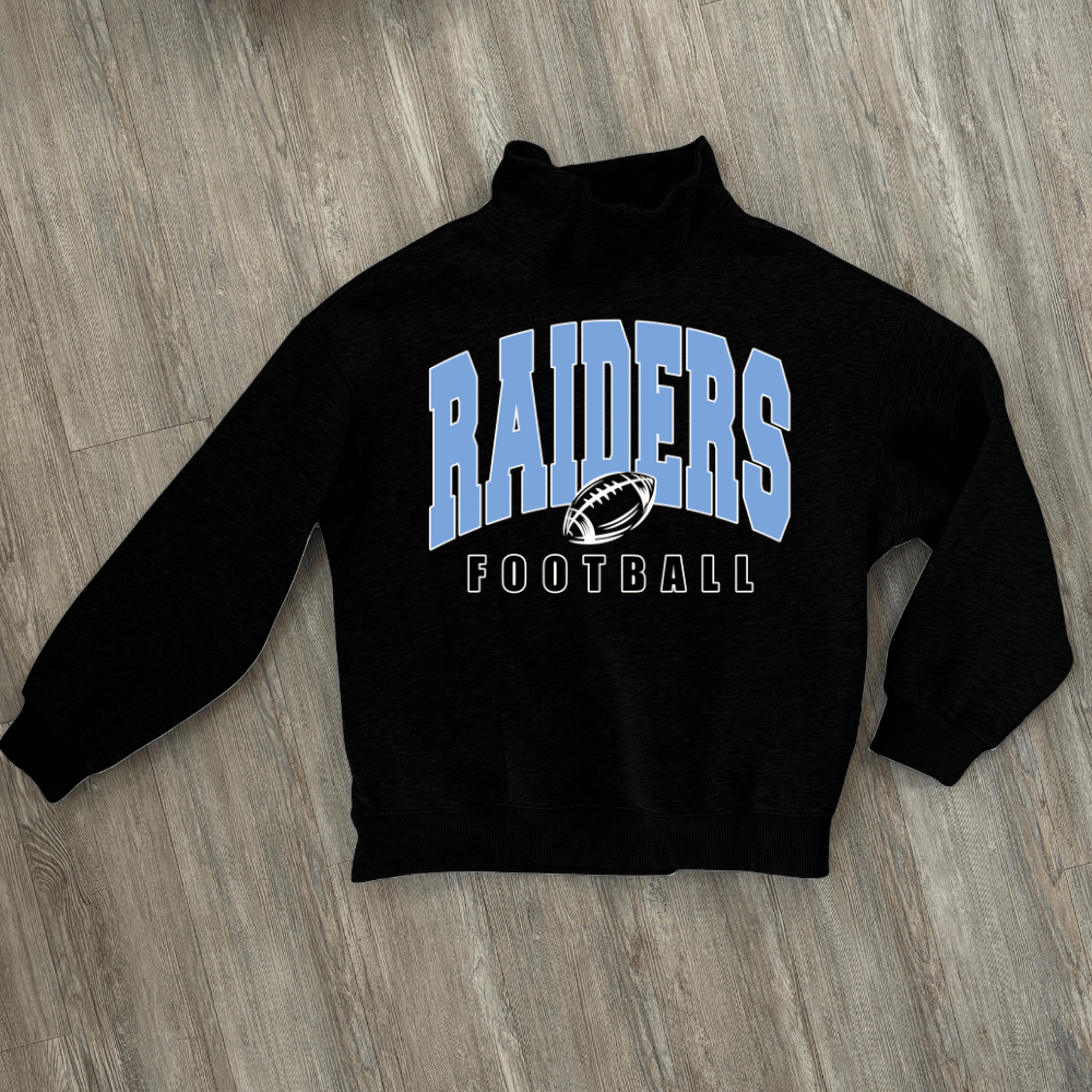 A black long-sleeve mock neck sweatshirt with 'RAIDERS FOOTBALL' printed on the front in light blue and white, laid flat on a gray wood-look floor.