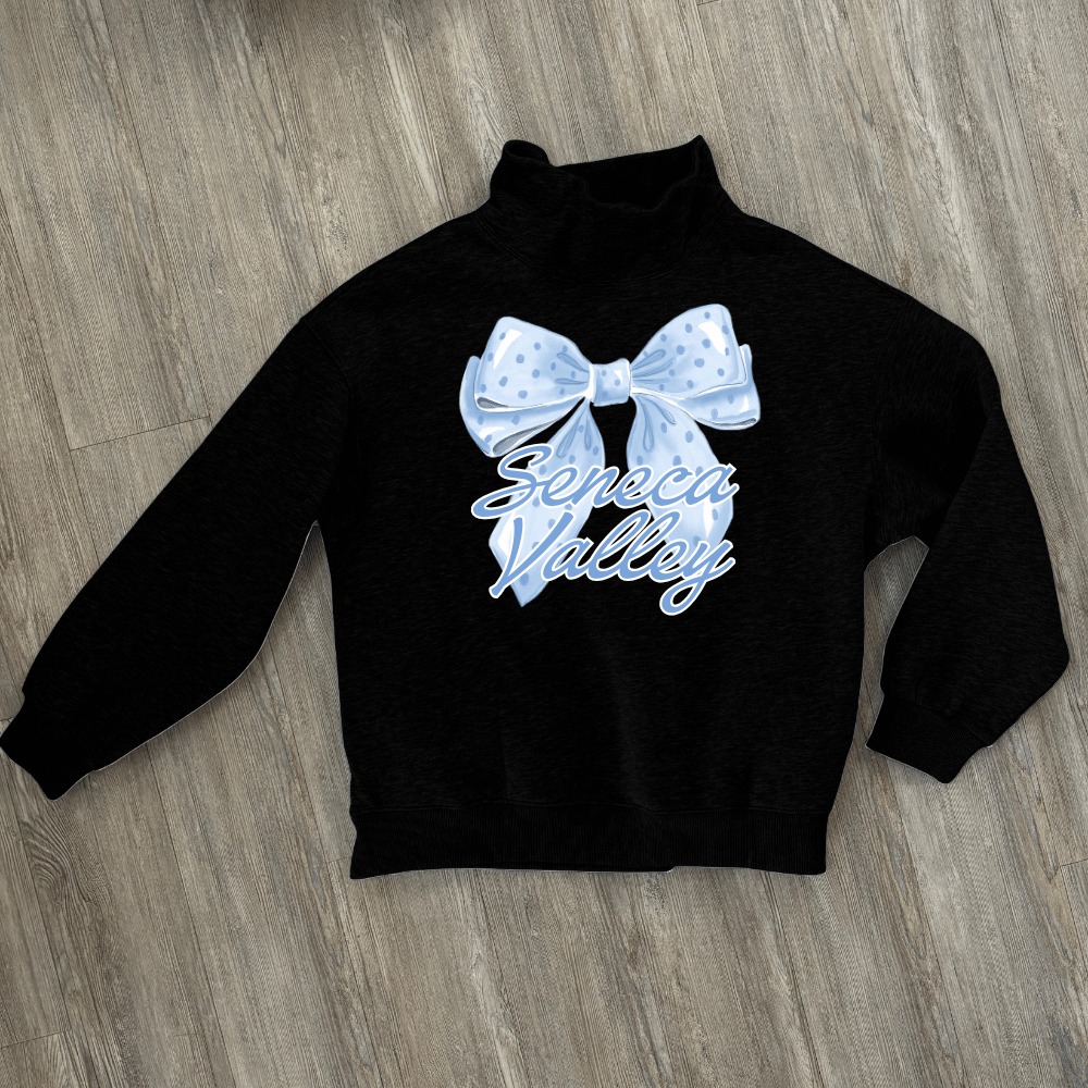 A black long-sleeve mock neck sweatshirt laid flat on a gray wood floor, featuring a light blue polka-dotted bow graphic and the words 'Seneca Valley' in light blue script across the chest.