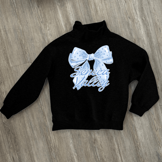 A black long-sleeve mock neck sweatshirt laid flat on a gray wood floor, featuring a light blue polka-dotted bow graphic and the words 'Seneca Valley' in light blue script across the chest.